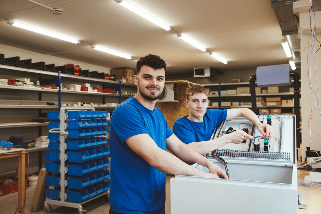 GROSS-Mitarbeiter-Mechatroniker-Kaeltetechnik-20260721-04 Zwei Mitarbeiter von GROSS Kälte-, Klima- und Wärmetechnik arbeiten gemeinsam an einem Schaltschrank in der Werkstatt in Rödelsee.